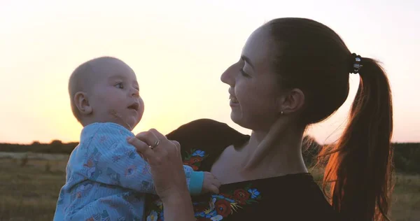 Счастливая молодая мать играет со своим ребенком в поле на закате — стоковое фото