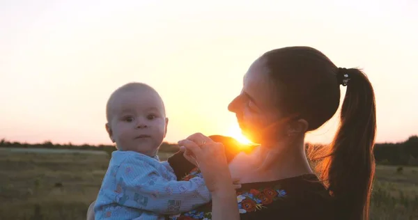 Felice giovane madre che gioca con il suo bambino in un campo al tramonto — Foto Stock