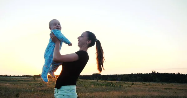 Счастливая мать с хвостиком воспитывает ребенка на большом поле на закате — стоковое фото