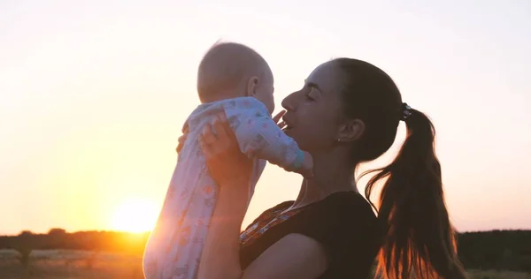 Счастливая молодая женщина целует своего ребенка в поле на закате . — стоковое фото