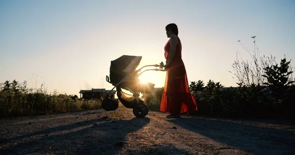 Ніжна жінка в червоній сукні, що гуляє зі своєю дитиною в колясці — стокове фото