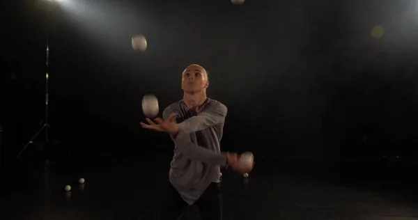 Juggler in the black studio make tricks with balls.