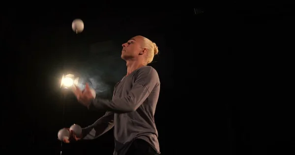 Жонглер в черной студии делает трюки с пятью шарами — стоковое фото