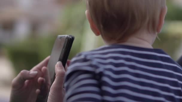 Niño de un año mira la pantalla del smartphone en las manos — Vídeo de stock