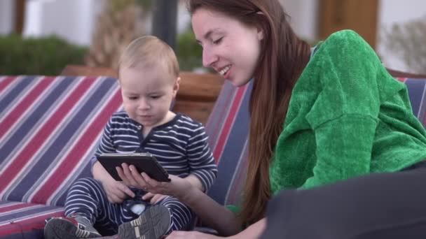 Flickan sjunger en sång till barnet och visar något för honom på smartphone — Stockvideo