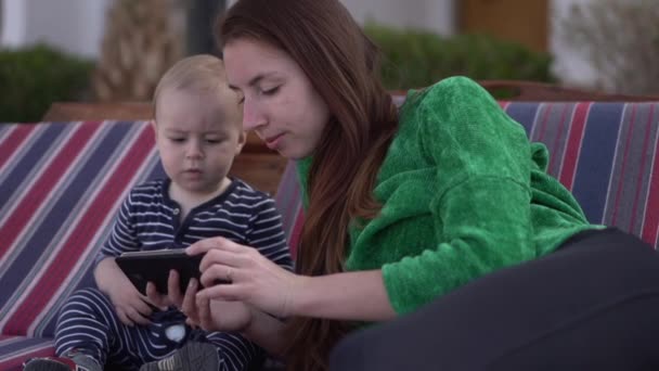 Mamma och baby tittar på något på telefonen med ett allvarligt ansikts uttryck — Stockvideo