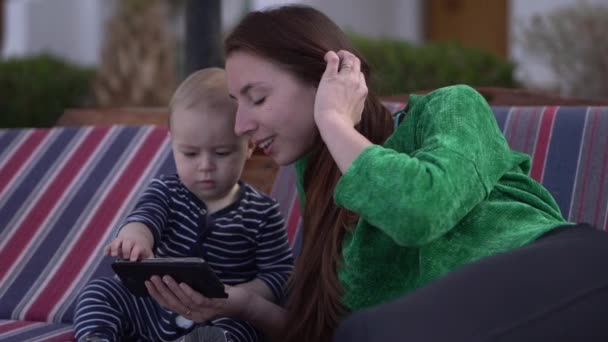 Barnet klickar på smartphone, sitter med sin mamma i slow motion. — Stockvideo