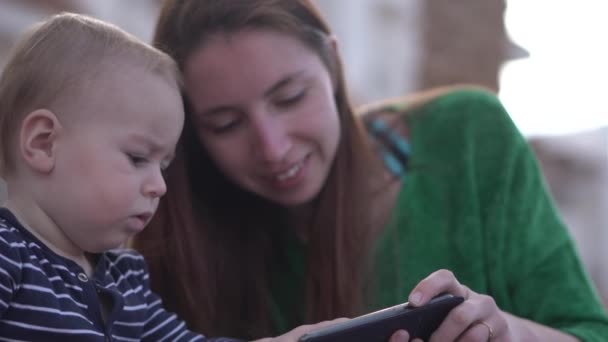 Пухкий серйозний малюк клацає смартфон, сидячи поруч з мамою в повільному русі крупним планом — стокове відео