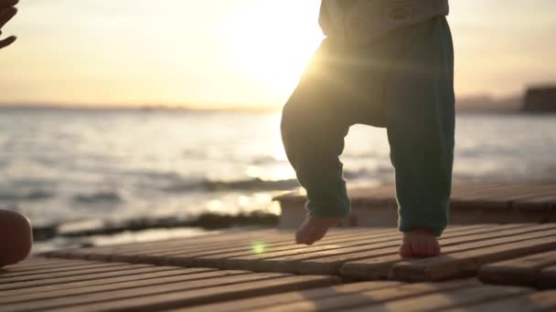 Les bébés petites jambes tamponnent sur les chaises longues pendant le coucher du soleil en mer au ralenti . — Video