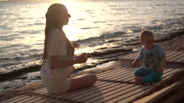 Fille et petit garçon dansant assis sur une chaise longue en bois au coucher du soleil . — Video