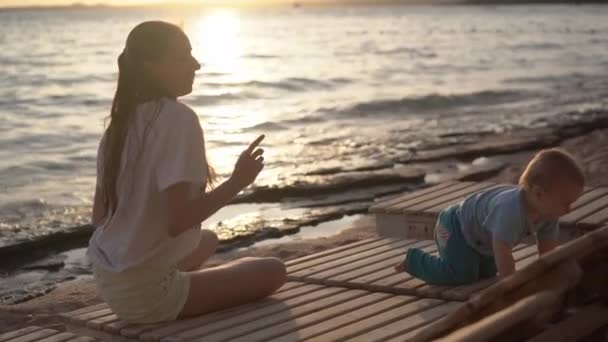 日落时, 妈妈和宝宝在海边的躺椅上慢动作地跳舞 — 图库视频影像
