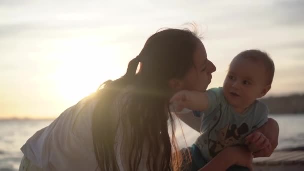 Mor kysser en baby, der viser noget med entusiasme nær havet i slowmotion – Stock-video