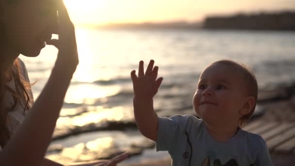 Happy Girl geeft High-Five aan de baby en kusjes hem bij zonsondergang in slow motion — Stockvideo