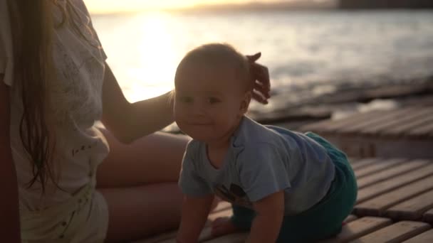 Девушка гладит голову маленького ребенка на вечернем пляже в замедленной съемке — стоковое видео