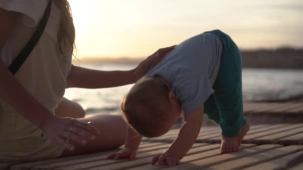 Un bébé mignon rampant sur une chaise longue en bois près de maman au ralenti — Video