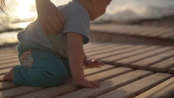 La madre hace cosquillas a un pequeño bebé cerca del mar al atardecer en cámara lenta — Vídeo de stock