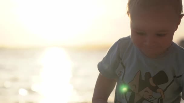 Pequeño bebé lindo camina por el mar durante el atardecer en cámara lenta — Vídeos de Stock