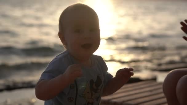 Een mollige schattige baby dansen op een ligstoel in de buurt van de avond zee in slow motion — Stockvideo