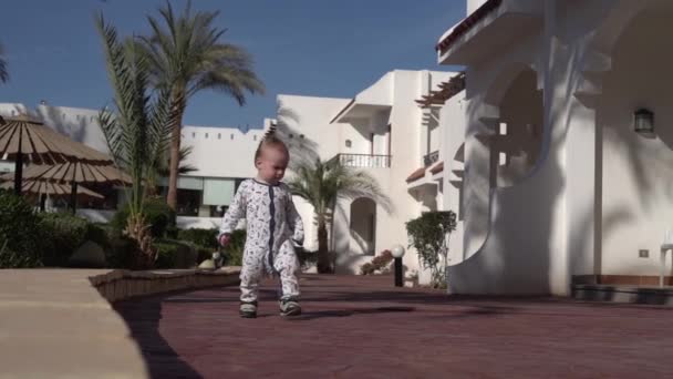 Un bambino di un anno cammina lungo un hotel tropicale al rallentatore — Video Stock