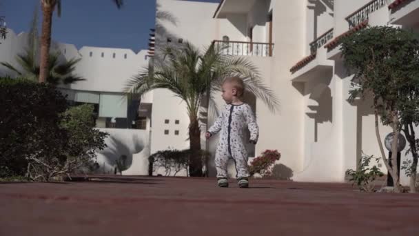 Kleine baby kijkt rond in de buurt van een tropisch Hotel in slow motion — Stockvideo