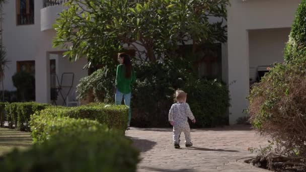 Küçük bebek yavaş hareket anne arkasındaki yol boyunca yürüyor. — Stok video