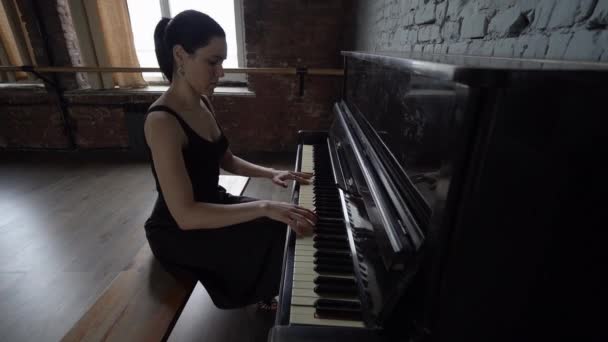 Una ragazza in abito nero si siede e suona il pianoforte - rallentatore . — Video Stock