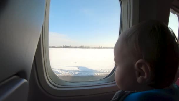 Καταπληκτικό ξανθιά μικρό αγόρι κάθεται κοντά στο παράθυρο του αεροπλάνου και φαίνεται. — Αρχείο Βίντεο