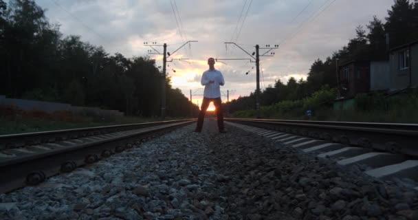 Cavalheiro malabarista ao pôr do sol faz truques na ferrovia . — Vídeo de Stock