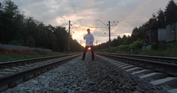 Cavalheiro malabarista ao pôr do sol faz truques na ferrovia . — Vídeo de Stock