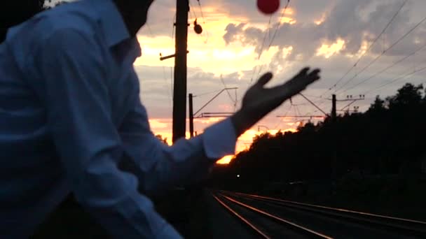 4k-zsonglőr a naplementében egyenlegek egyik lábát a vasút közelében, és teszi a veszély trükk. — Stock videók
