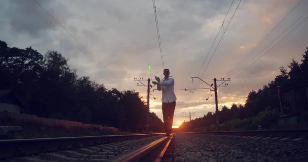 Gentalman artist makes trick on the railway at sunset. — Stock Photo, Image