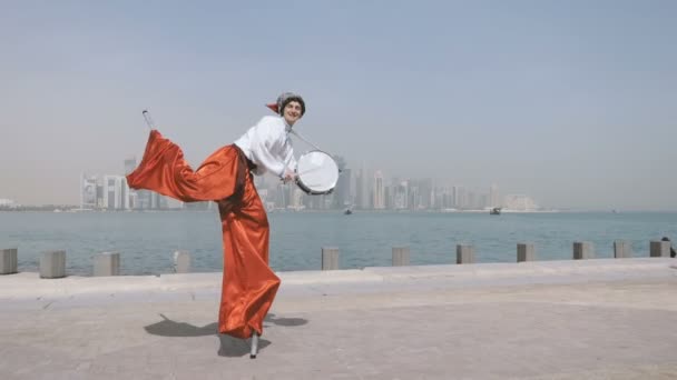 Веселый человек в украинском костюме танцует на ходулях с барабанами на открытом воздухе в сло-мо — стоковое видео