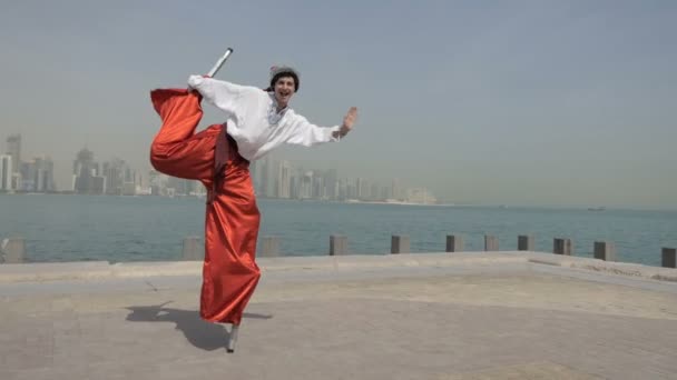Lycklig man i kosack kostym hoppar på en stylta på en sjökaj i Dubai i slo-mo — Stockvideo