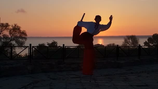 Artista en traje popular ucraniano bailando en zancos en la playa del mar al atardecer en slo-mo — Vídeo de stock