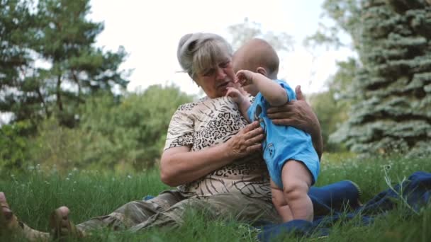 Cheery baby playing with his grandmother on a green lawn in slo-mo — Stock Video