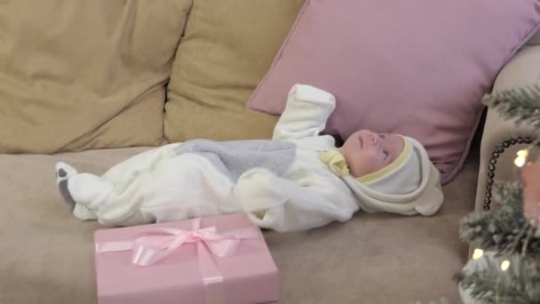 生まれたばかりの赤ん坊がクリスマスツリーの近くのソファーに横たわっている. — ストック動画