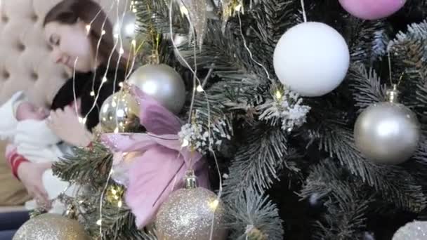 Geweldig schot van kerstboom en moeder met een pasgeboren baby op haar handen. — Stockvideo