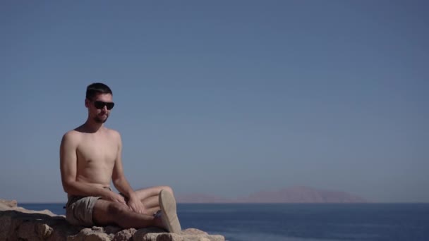 4k - man op zonnebril maakt yoga op het strand van de Oceaan. — Stockvideo