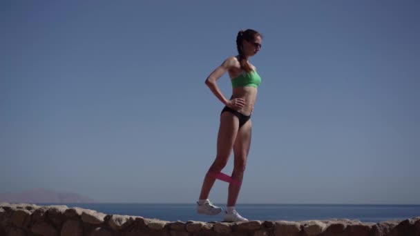 Sexy joven modelo hace ejercicios con goma para hermosas nalgas . — Vídeo de stock