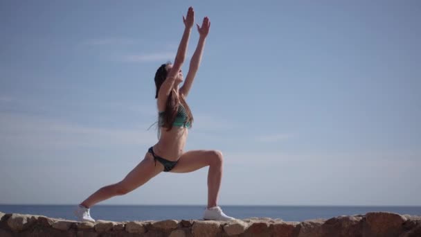 Slender sporty woman makes yoga pose warrior on the beach. — Stock Video