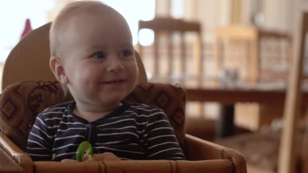 4k Pequeño bebé se sienta en la silla de bebé y come comida . — Vídeos de Stock