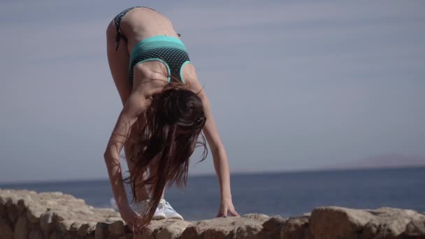 4k - Menina faz prática de ioga na pedra da praia do oceano . — Vídeo de Stock