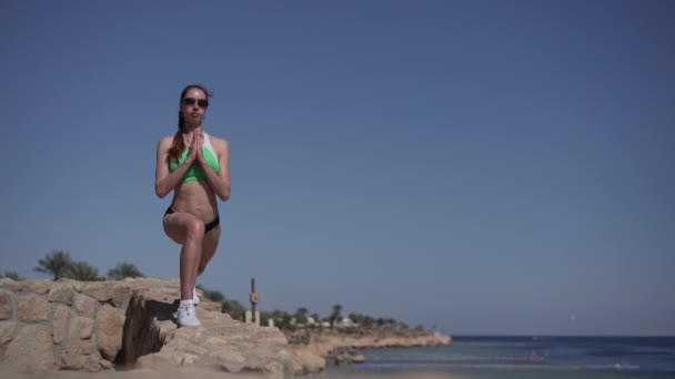 Meisje in zonnebrillen maakt yoga poseren op het strand. — Stockvideo