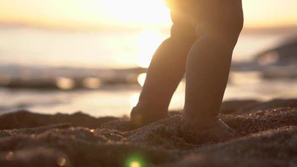 Amazing benen van de baby die stappen op het zandstrand bij zonsondergang maakt. — Stockvideo