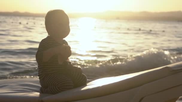 Funny and cute action - little kid sits on the lounger and falls on the back. — Stock Video