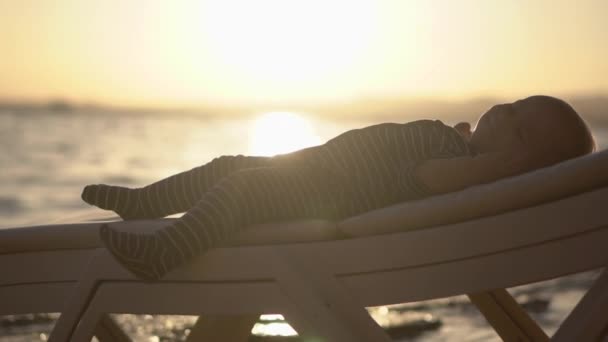 Ανάπαυση μωρού στην ξαπλώστρα στο ηλιοβασίλεμα σε αργή κίνηση. — Αρχείο Βίντεο