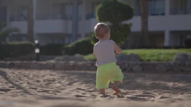Pequeño bebé caminar con bola en sus manos en cámara lenta en la playa . — Vídeos de Stock