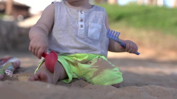 Mignon petit bébé joue sur la plage avec pagaie, râteau et sable . — Video
