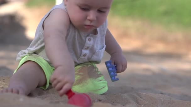 Lindo bebé juega en la playa con paleta, rastrillo y arena . — Vídeo de stock