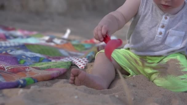 Söt liten bebis leker på stranden med paddel, rake och sand. — Stockvideo